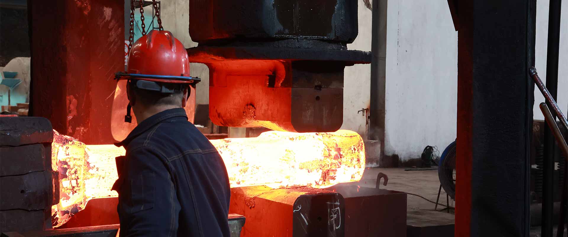 Factory scene showing a glowing steel billet being handled during hot forging.